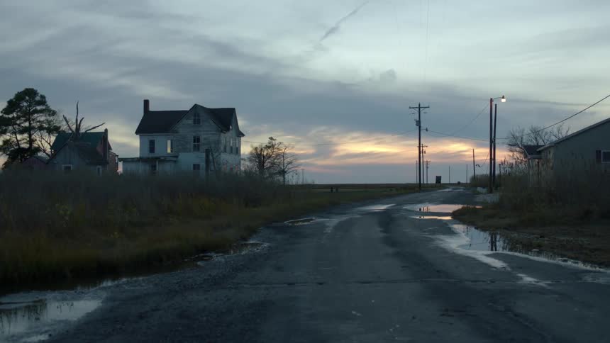 A flooded rural street at sunset with a long road into the distance