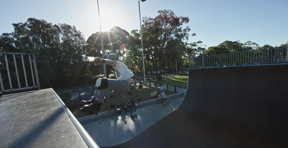 Man wearing skates jumping a skate ramp in a park at sunset
