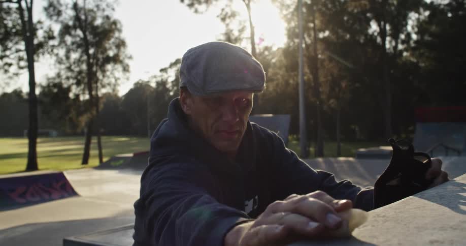 Man wearing golf cap runs object over skate area of park