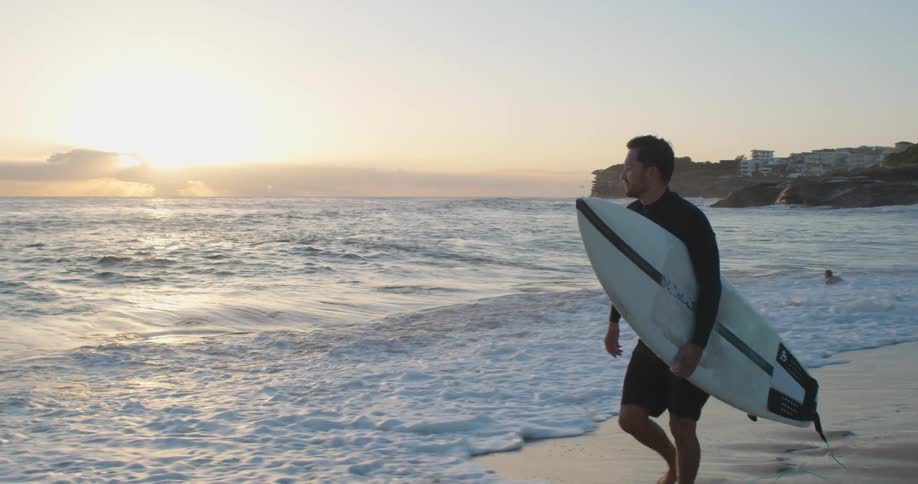 A man walking next to the ocean carrying a surfboard