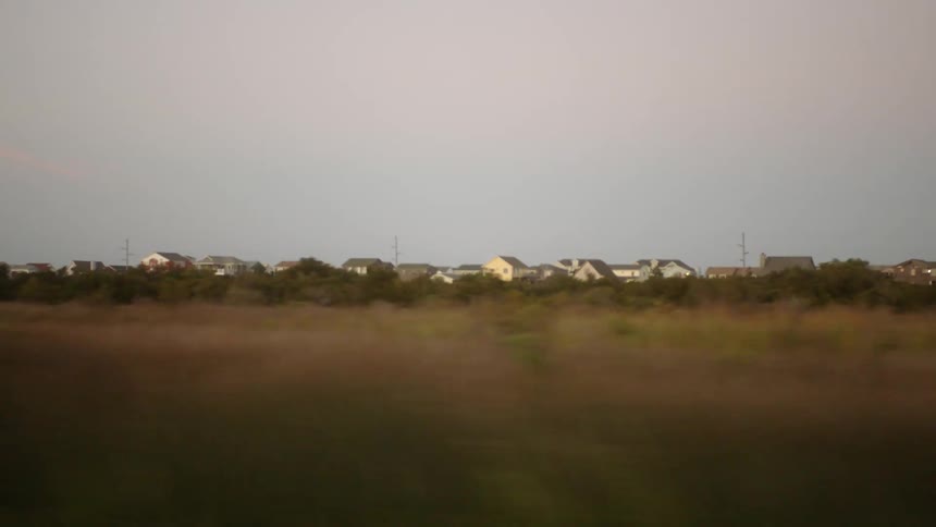 A landscape with grass and trees with houses the sky and clouds in the background