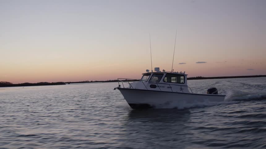 A boat traveling across the water at sunset with land in the background