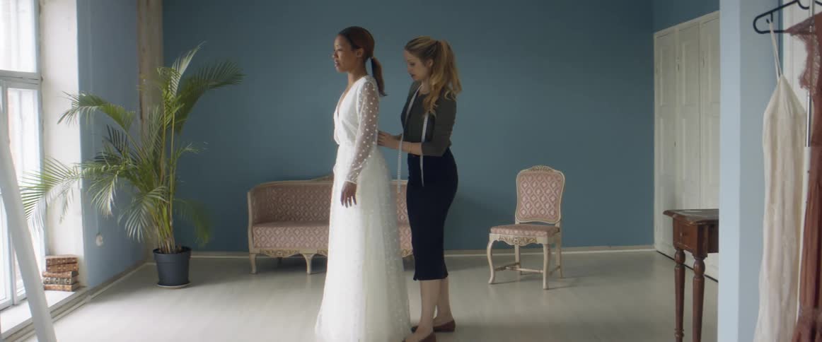 A woman is helping her friend try on a wedding dress