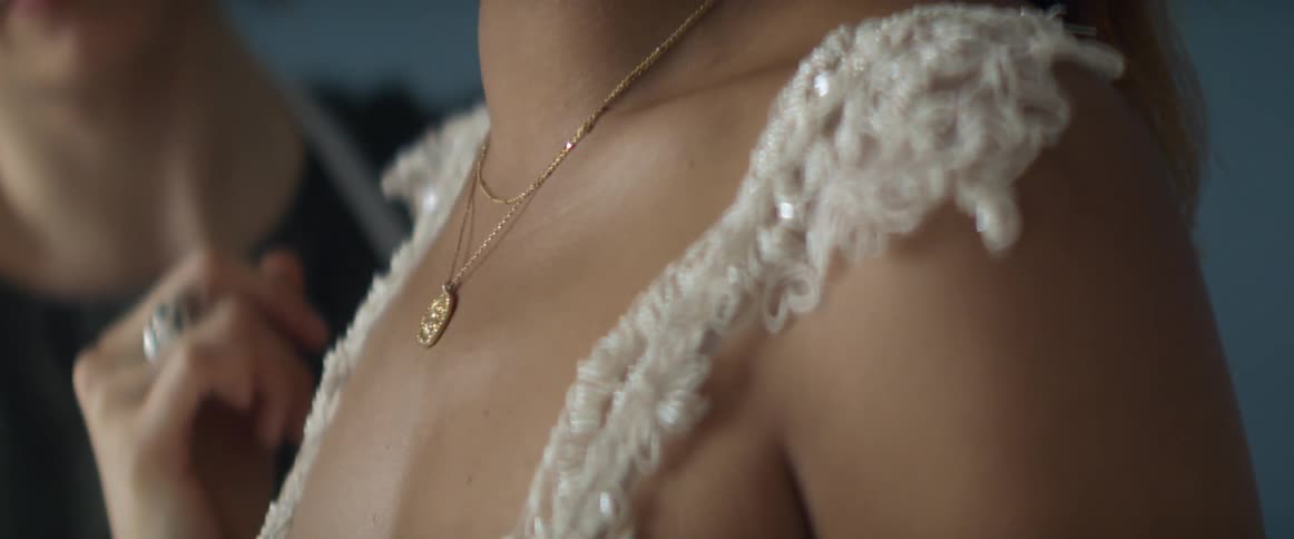 Seamstress adjusts necklace worn by woman trying on wedding gown