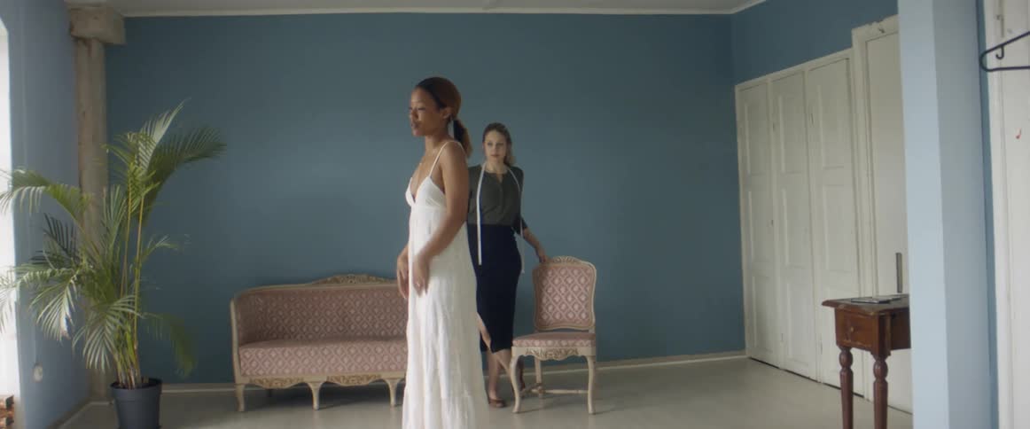 Tailor looking at a client testing a white long dress in her studio