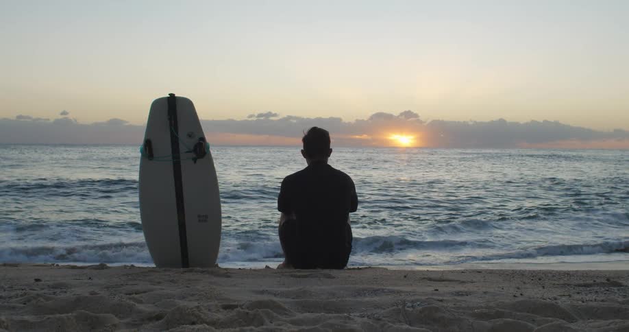 A man is sitting at the beach at dusk
