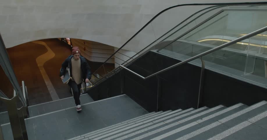 Young man carrying a skateboard walking up the stairs of a metro station