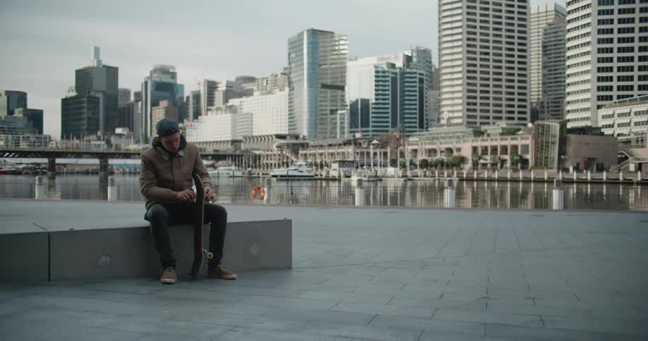 A man is sitting on the boardwalk with his skateboard spinning a wheel