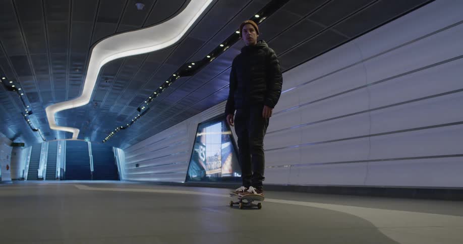 Man wearing coat at knit hat rides skateboard away from staircase leading to ground level hoping and turning in a trick