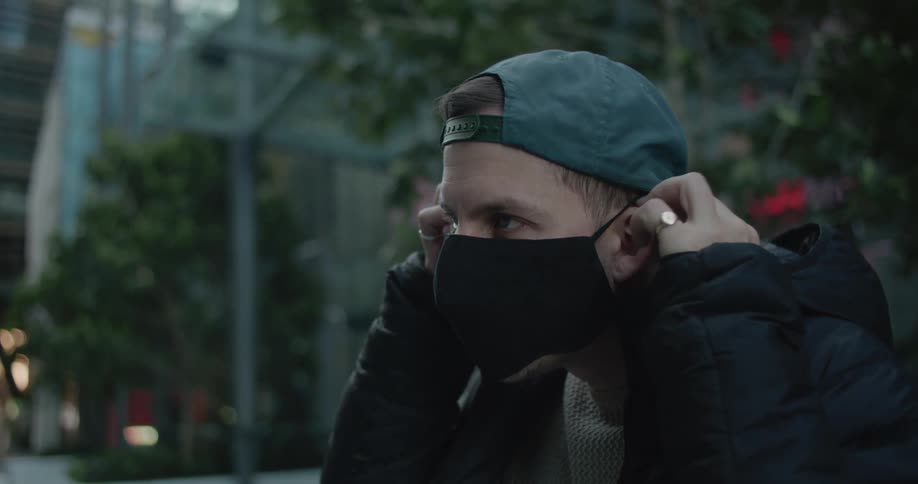 A man sitting on a city bench wall with his skateboard puts his mask on