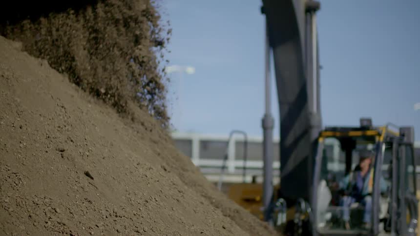 A backhoe dumps dirt onto a pile at a construction site
