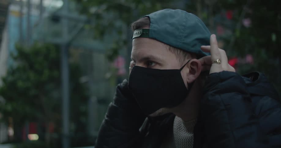 A man with a skateboard putting on a mask with trees and a building in the background