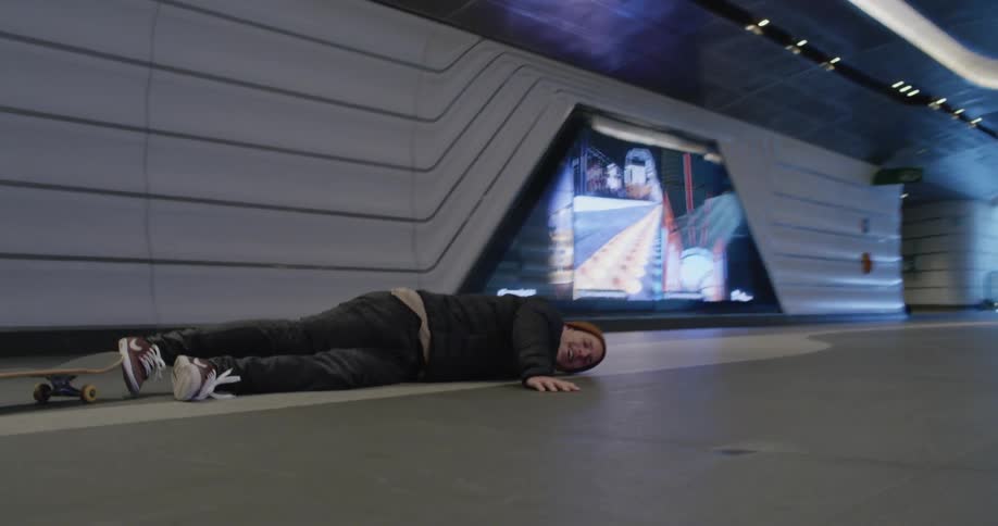 A man laughs after falling off a skateboard while riding in a subway station