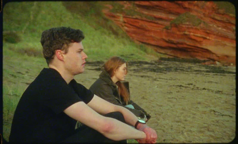 A young woman glances over at the young man sitting next to her at the beach