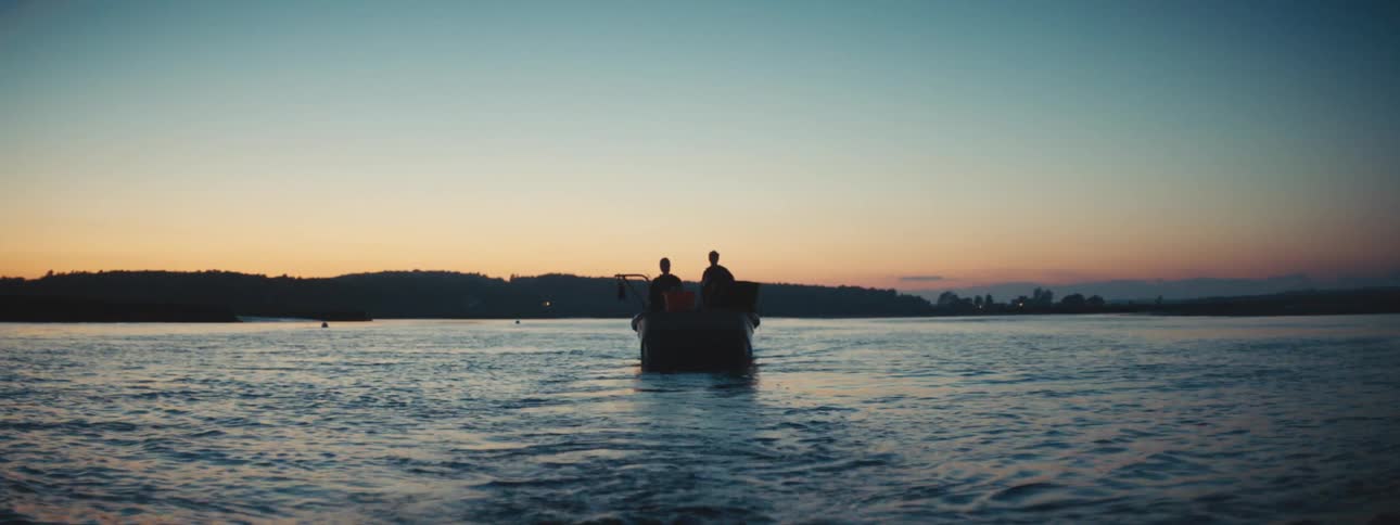 Two people riding a boat on the calm surface of a lake at sunset