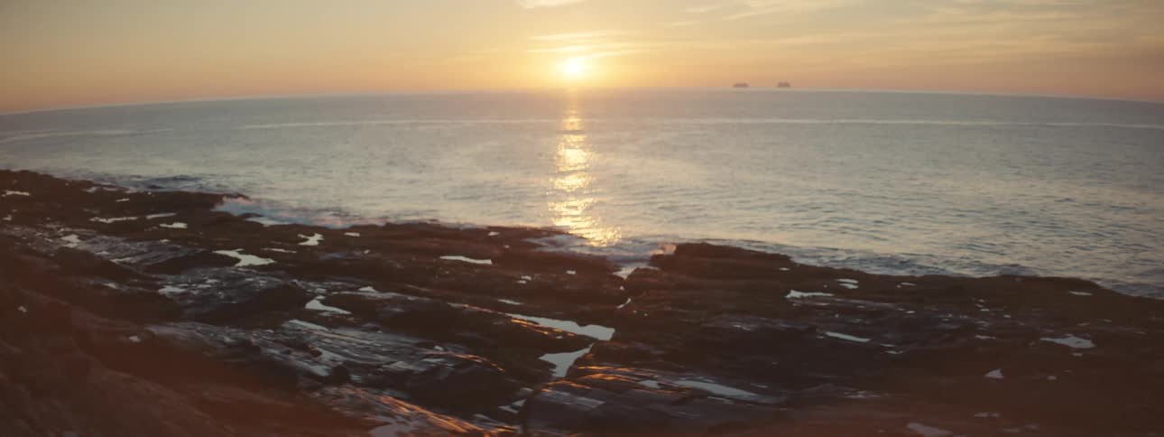 The sun is low in the sky above where the ocean meets a rocky coastal shoreline