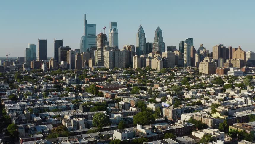 Neighborhood streets and rooftops sprawl in front of a towering city skyline