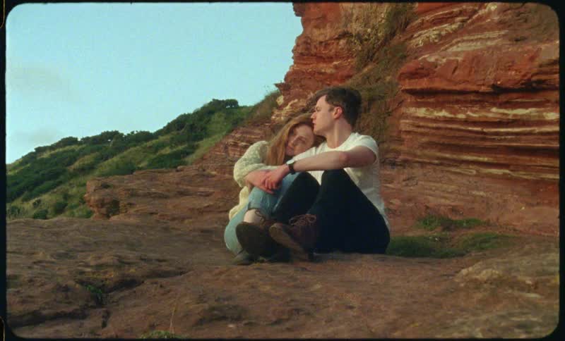 A woman rests her head on a mans shoulder as they sit on a ledge