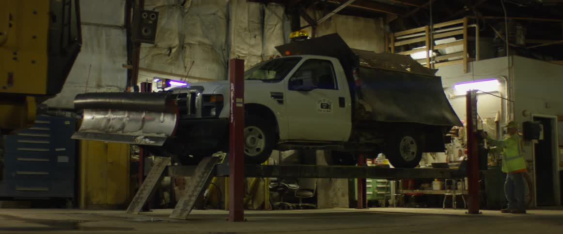 A mechanic lowers a truck with a plow on a lift at an automotive garage