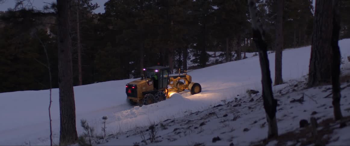 Snowplow plows the snow from the road near the forest at night