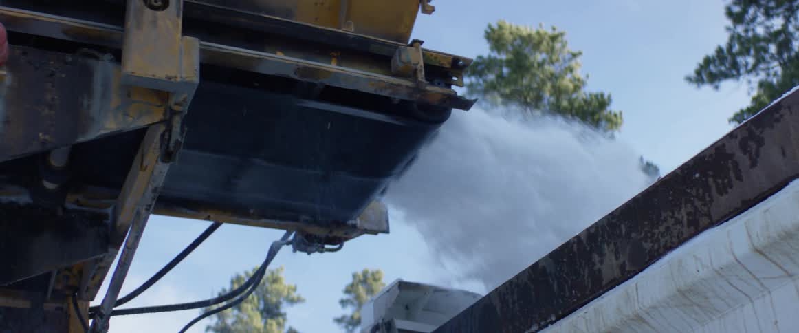 Conveyor belt fills truck bed with white snow