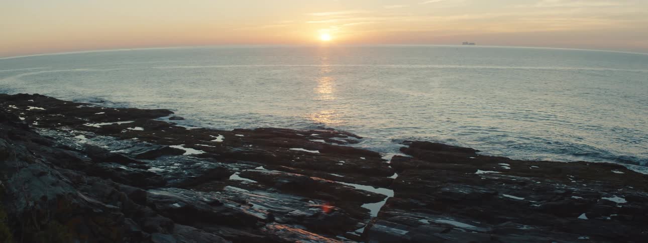 A rocky shore with the ocean the sunset the sky and clouds in the background