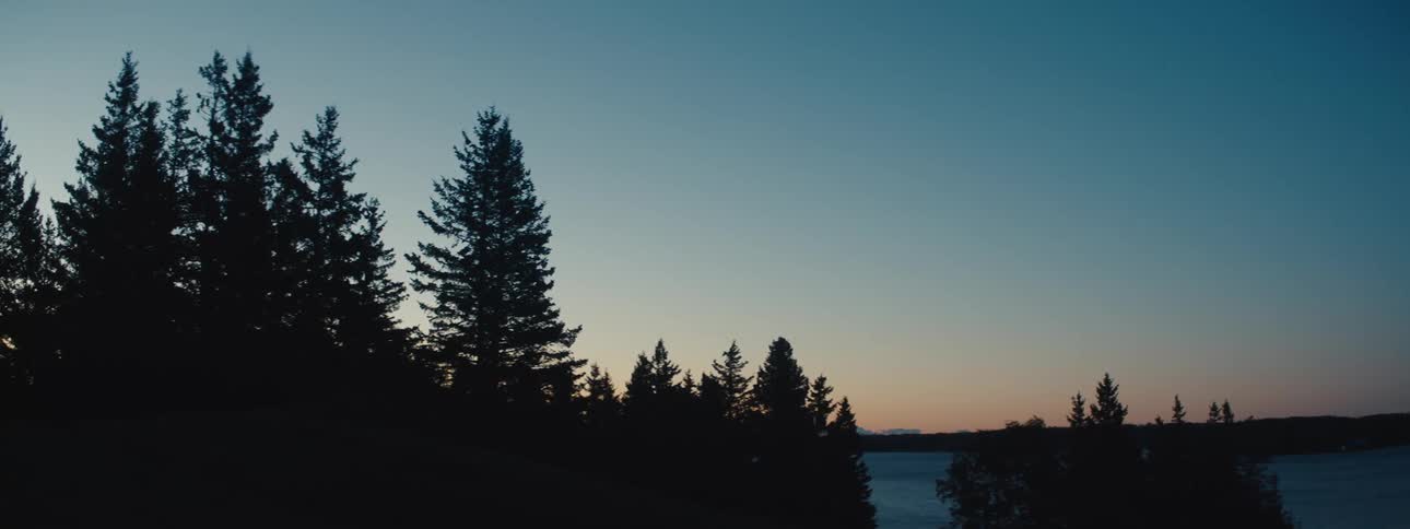 The sun sets over a forest and adjacent lake