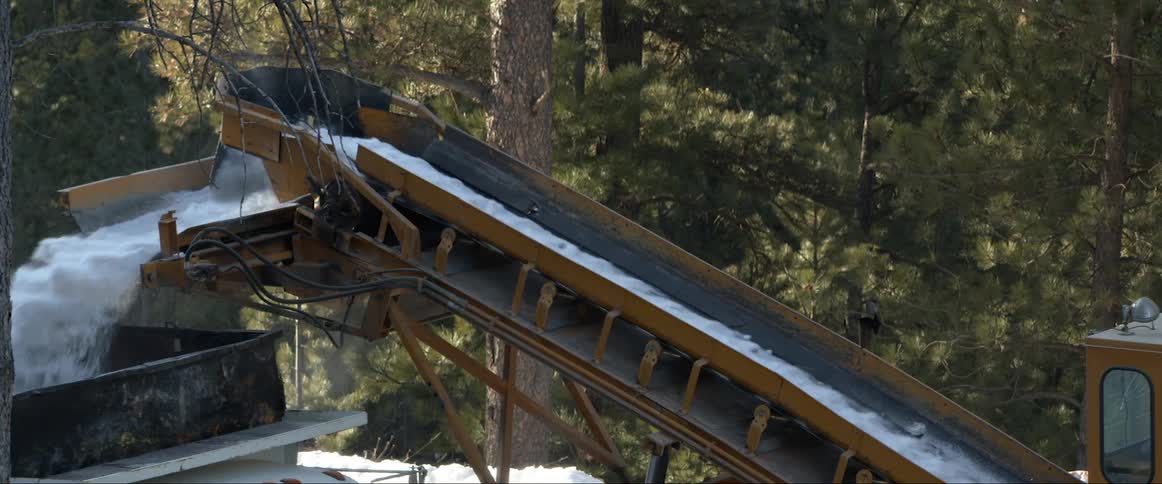 Snow being moved on a construction conveyor outdoors during the day