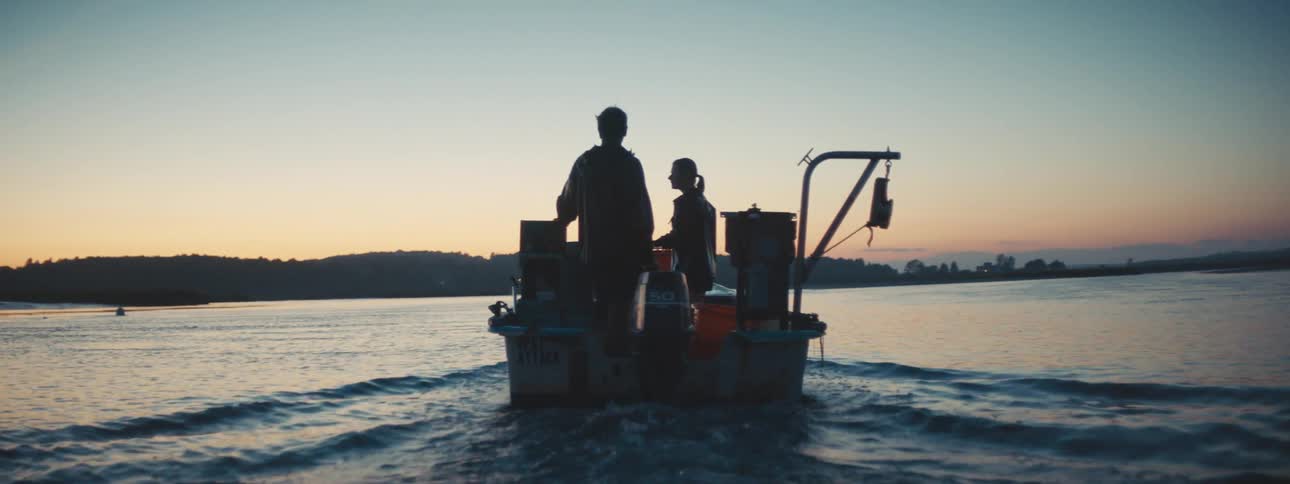 Silhouettes of two people on a small boat moving out in the ocean at sunset