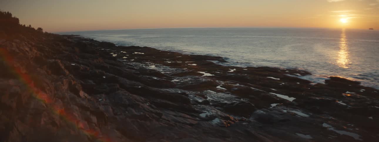 A rocky shore with the ocean the sunset the sky and clouds in the background
