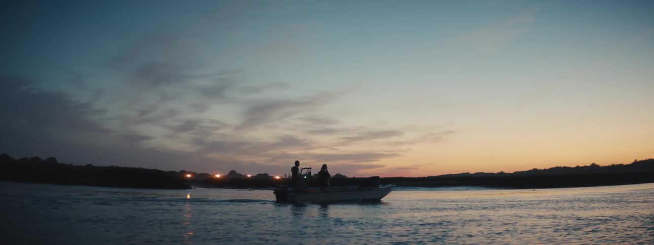 Silhouette of two people on a boat out in the ocean close to land in the evening