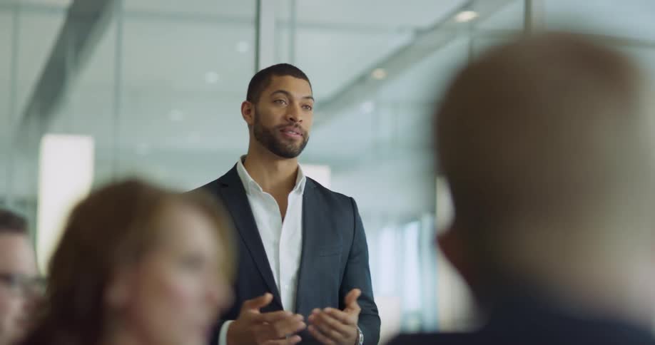 Man with a beard stands and laughs and talks with people sitting in an office