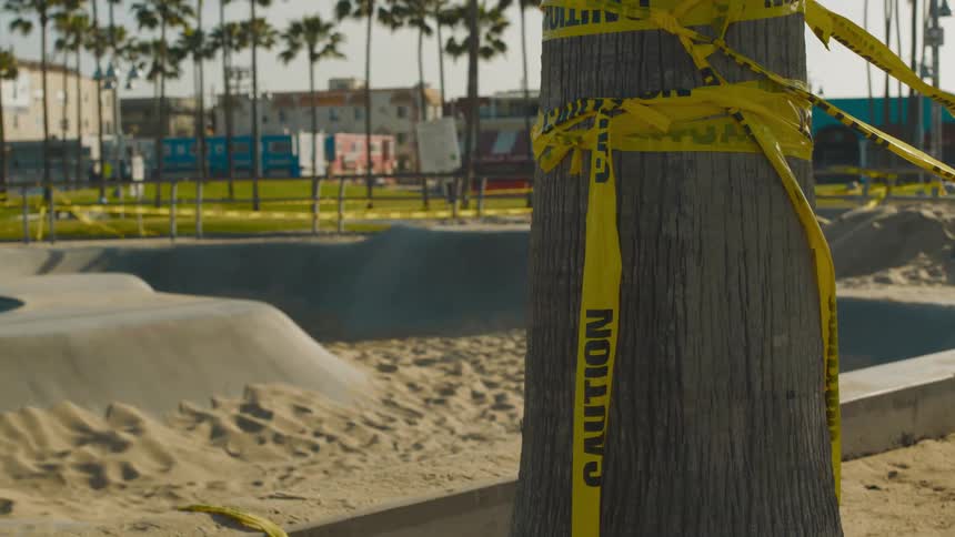 Yellow caution tape surrounds sand filled construction site in park with apartment buildings in background