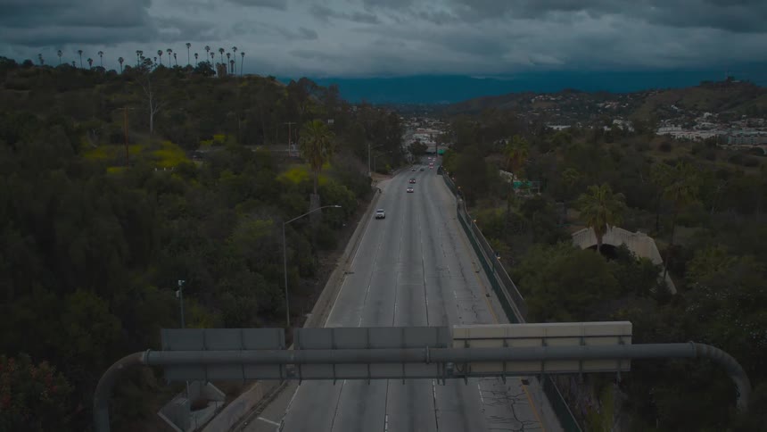 Cars drive along road under highway signs away from town
