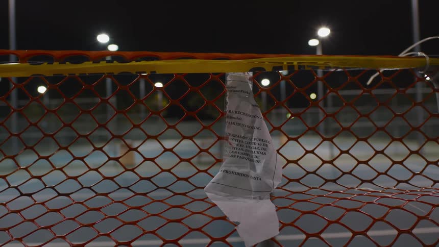 A tattered paper notice hangs from a temporary plastic fence around outdoor tennis courts