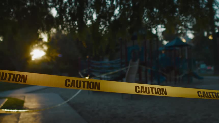 A playground with caution tape with trees the sky and clouds in the background