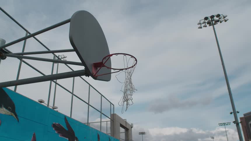 A torn basketball net hangs from the backboard at a park