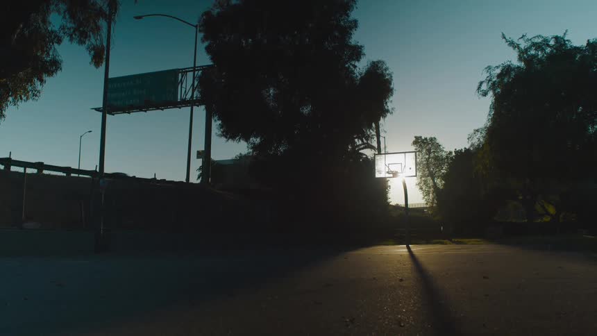 Sunlight shining behind an outdoor basketball hoop with cars driving by