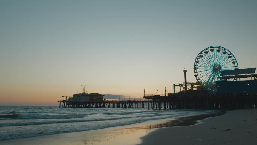 A ferris wheel at an amusement park on the pier at sunset