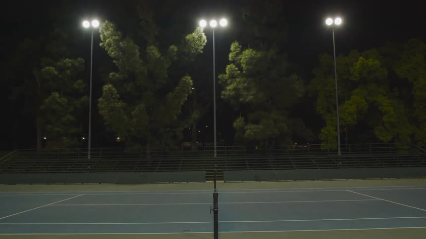 Car headlights light up driving past a tennis court at night