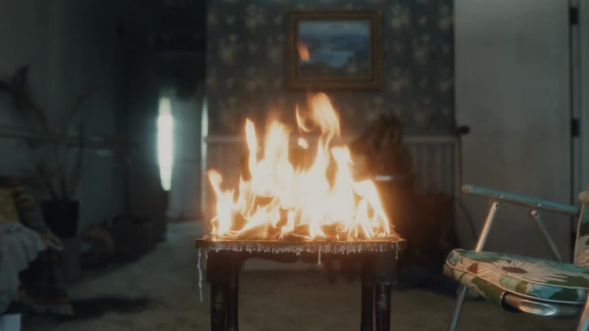 A table in a room on fire with a wall and doorway in the background