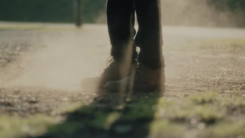 A person wearing boots is dancing skillfully in a dusty dirt covered outdoors area