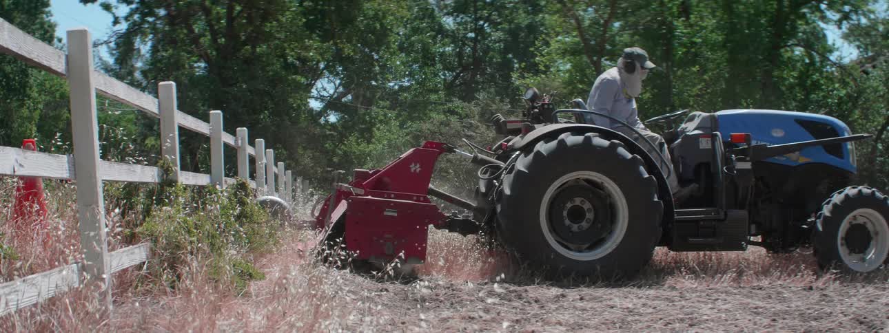 A person drives a tractor away from a fence while turning the soil