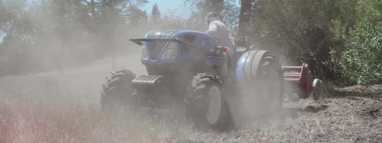 A person with gloves on a tractor with trees the sky and clouds in the background