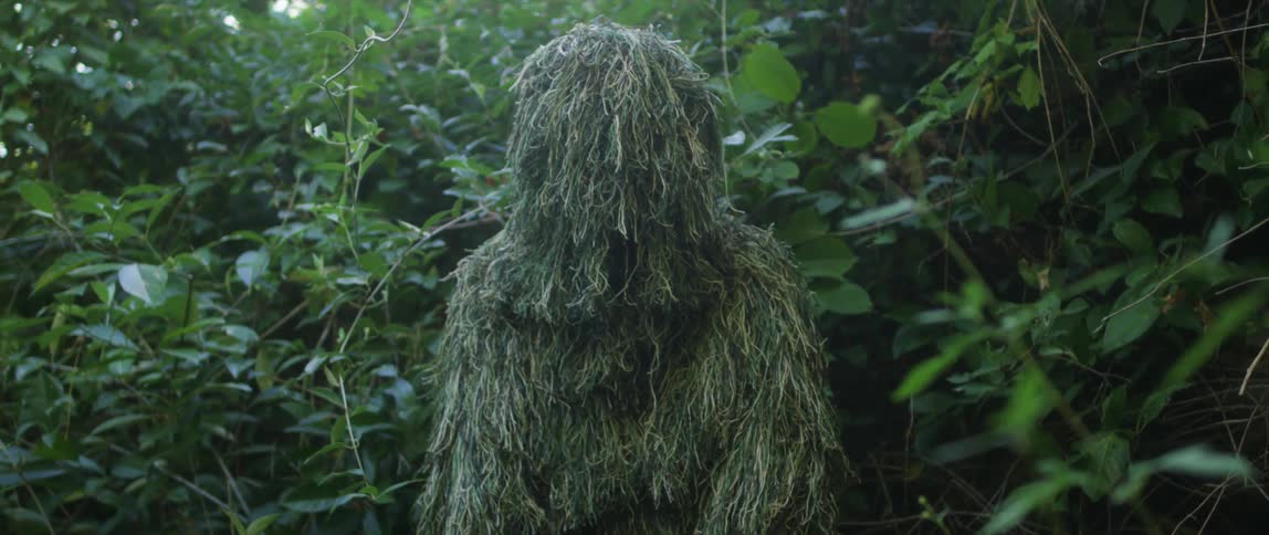 A person is standing in a jungle and wearing camouflage