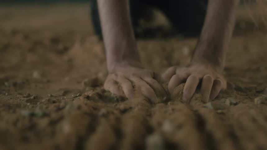 A man runs his hands through soil