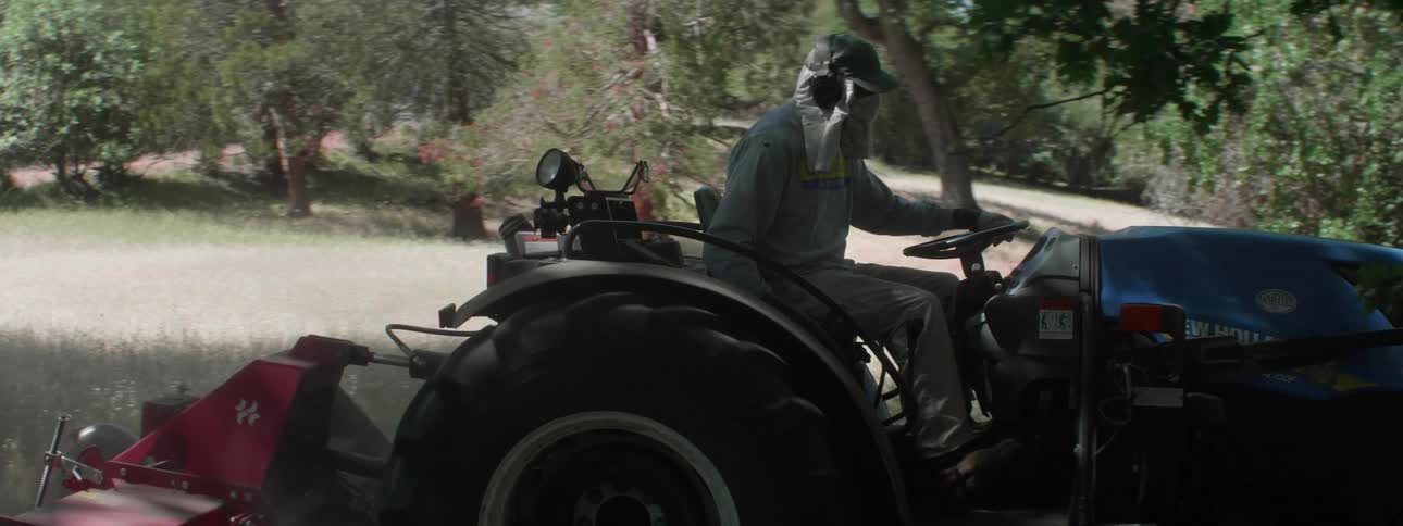 A farmer plowing a rural grassy field on a summer day
