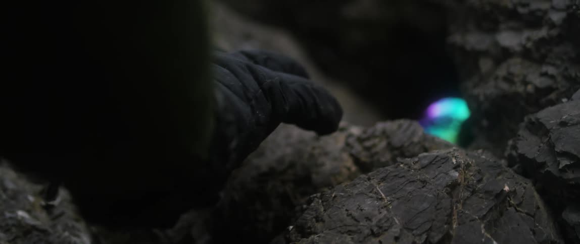 A gloved hand approaches a glowing object