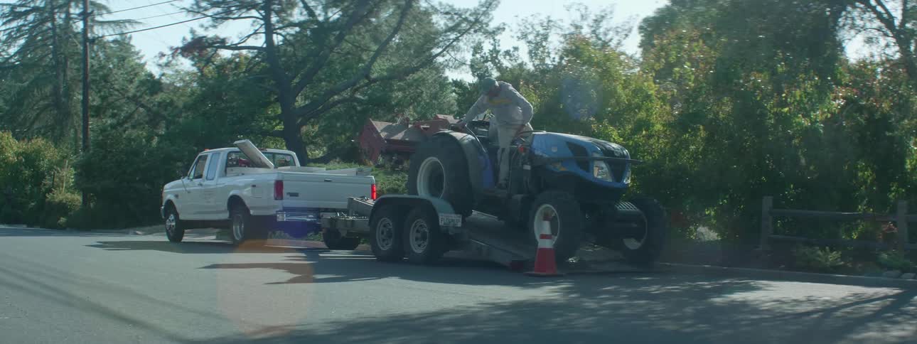 Man drives tractor backwards loading it onto a trailer behind a pickup truck