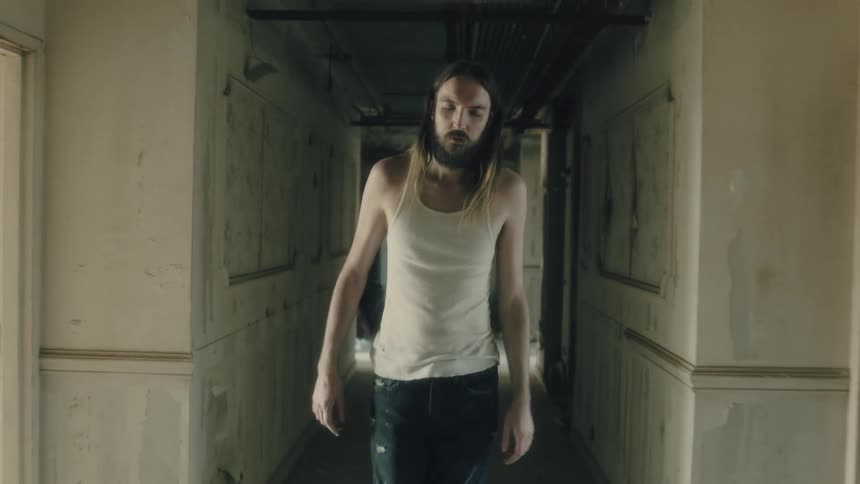 Man passes woman as he walks down hall of worn building gesturing